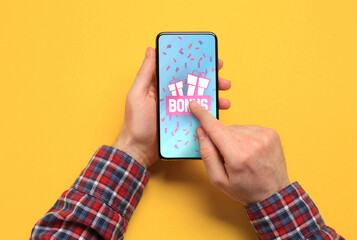 Bonus gaining. Man using smartphone on yellow background, top view. Illustration of gift boxes,...