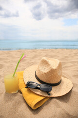 Straw hat, sunglasses, towel and refreshing drink on sandy beach near sea. Space for text