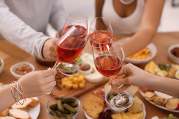 People clinking glasses with rose wine above wooden table indoors, closeup