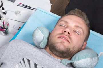 A handsome young man with his eyes closed lies and applies eyelashes. Eyelash lamination agent...