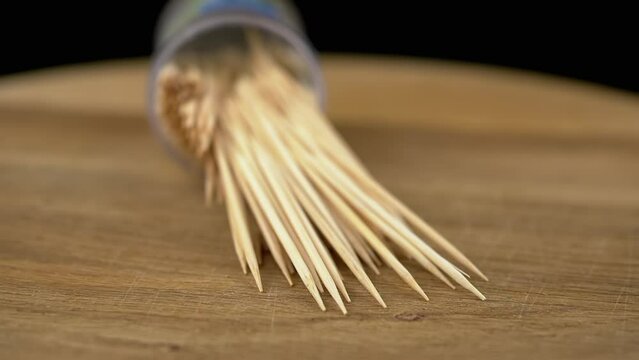 Scattered Toothpicks Rotate on a Wooden Background. Close up. A set of bamboo wooden toothpicks in a plastic cup. Home oral care after meals. Teeth cleaning. Blurred motion. Dentistry concept. Loop.