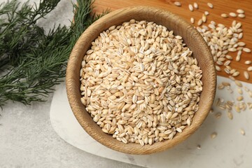 Dry pearl barley in bowl and dill on table, top view