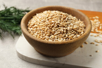 Dry pearl barley in wooden bowl on table, closeup