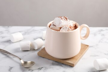 Cup of aromatic hot chocolate with marshmallows and cocoa powder served on white marble table