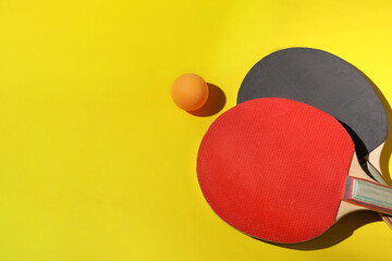Ping pong ball and rackets on yellow background, flat lay. Space for text