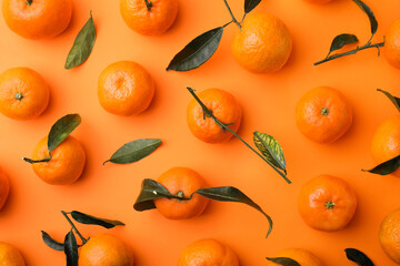 Fresh ripe tangerines with green leaves on orange background, flat lay