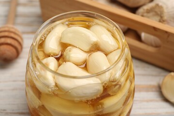 Honey with garlic in glass jar on light table, closeup
