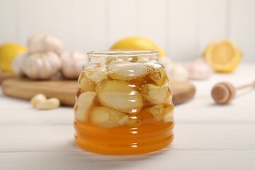 Honey with garlic in glass jar on white wooden table