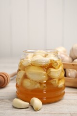 Honey with garlic in glass jar on light wooden table