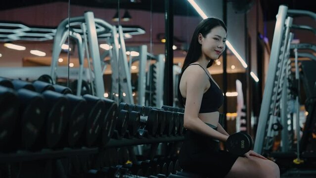Black dumbbell row set. Young asian woman holding metal dumbbells on rack in sport fitness gym, Weight training equipment