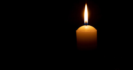 Single burning candle flame or light glowing on big white candle on black or dark background on...