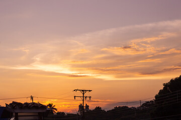 Naklejka premium Silhouette of electric pole at sunset with orange sky background.