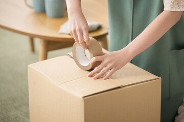 Woman's hand putting duct tape on cardboard boxes when packing for a move Faceless