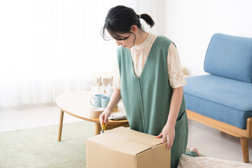 A young woman unpacking cardboard boxes with a cutter after the move. - obrazy, fototapety, plakaty