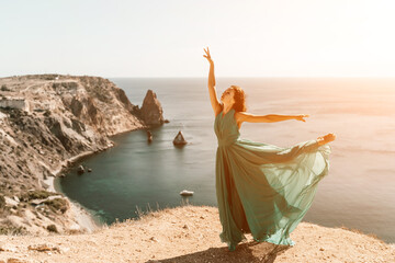 Fototapeta na wymiar Woman green dress sea. Female dancer posing on a rocky outcrop high above the sea. Girl on the nature on blue sky background. Fashion photo.