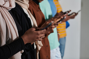 A diverse group of students, immersed in the digital age, stands united while engaging with their smartphones against a white backdrop, symbolizing the modern era of connectivity, communication, and