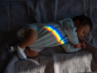 Top view of a sleeping newborn boy with a prism beam on his body. Rainbow.