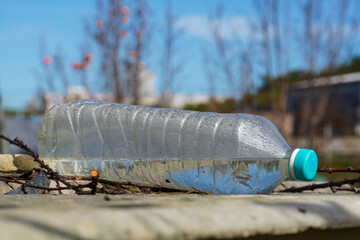 Fototapeta premium Littered plastic water bottle with blue cap lying outdoors. Environmental pollution.