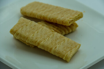 Close-up of stacked crispy, light brown wafer biscuits with visible layers, presented on a white surface. Sweet snack detail.