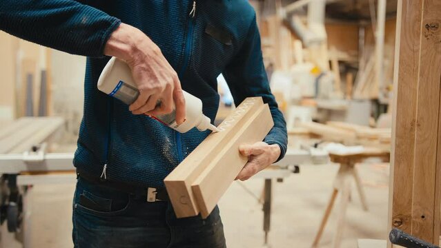Carpenter putting glue onto piece of wood before joining it to window frame in workshop - shot in slow motion