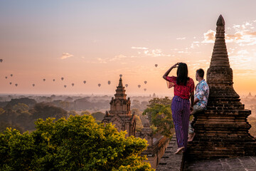 Bagan Myanmar, a couple of men and women are looking at the sunrise on top of an old pagoda temple. a couple on vacation in Myanmar Asia visit the historical site of Bagan with hot air balloons  - obrazy, fototapety, plakaty