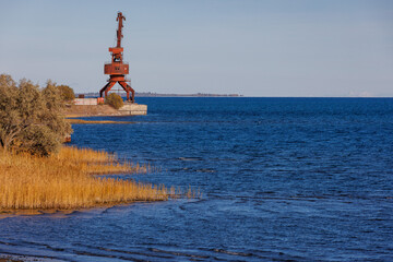old rusted dock crane on mountain lake Issyk-Kul at sunny autumn afternoon.