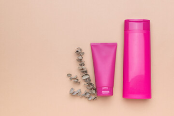 Two bottles for cream and shampoo and a sprig of eucalyptus on a beige background.