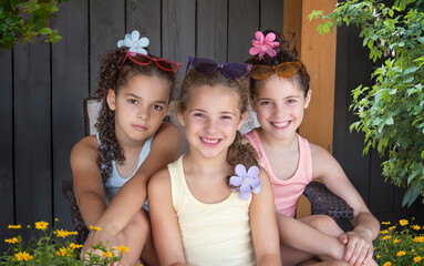 Three little girls wearing retro sunglasses and tank tops relaxing and sitting outside - 694227834