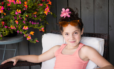 Pretty little girl with pink flower barrette in hair sitting outside with orange sunglasses on head  - 694227852