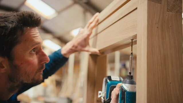 Carpenter using attachment on electric power drill to fasten piece of wood to window frame in workshop - shot in slow motion