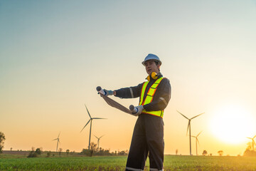 Male engineer in uniform wearing helmet sits and monitors wind turbine station operation holding...