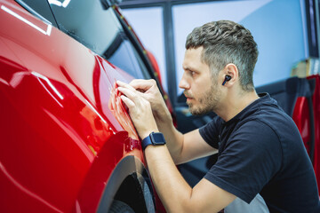 Naklejka premium The process of installing protective film on the new red car.