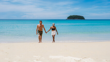 Fototapeta na wymiar Mature couple walking on the beach of Kata Phuket Thailand during vacation, happy men and woman on vacation holidays in Thailand walking by the ocean of Kata Beach Phuket
