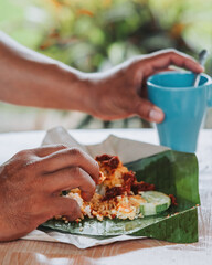 An asian hand eating Nasi Lemak with a mug on the side. Staple breakfast for Malaysian.
