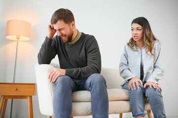 Couple arguing. Wife shouting to her desperate husband sitting on a couch in the living room at home