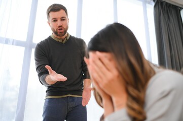 Irritated husband is shouting at his wife with violence. Woman is covering her face with fear