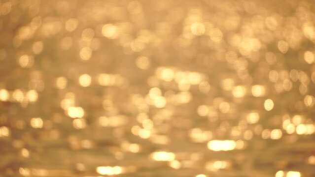 Blurred golden sea at sunset. The sun reflects and sparkles on the waves with bokeh, illuminating the golden sea. Holiday recreation concept. Abstract nautical summer ocean sunset nature background.