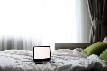 Laptop with blank copy space screen display in bed with plaid, pillows against white wall. Aesthetic morning composition. Freelancer, outsourcing minimalist home business, work concept.