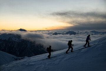 Silhouettes of three skiers with poles going up the slope
