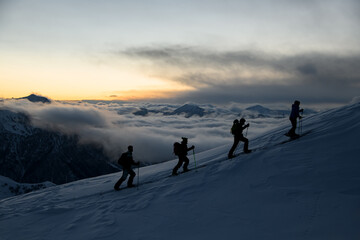 Silhouettes of four skiers with poles walking down the slope