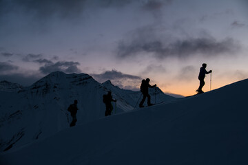 Silhouettes of four skiers on the highest point of the mountain massif after sunset