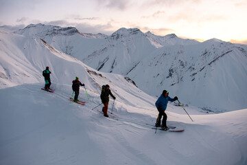 Four skiers climb slope after, the sun begins to rise