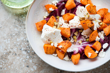 Beige plate with roasted sweet potato, fresh radicchio, feta cheese and chopped pistachios, closeup, horizontal shot