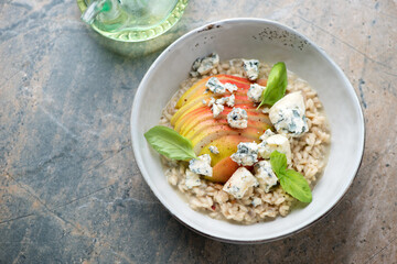 Grey bowl with pear and blue cheese risotto, horizontal shot on a grey and beige granite background with space, elevated view