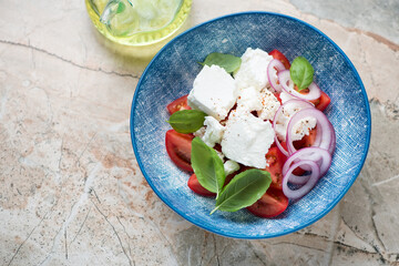 Blue plate with tomato, feta, red onion and basil salad, horizontal shot on a pinkish granite background with space, elevated view