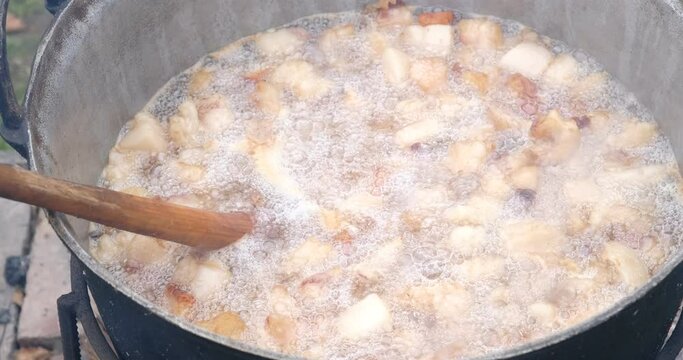 Preparation of delicious unhealthy fried pork greaves in a cauldron on the open fire. Delicious fried pork greaves in the pan traditional Romanian Christmas dish. Crispy deep fried