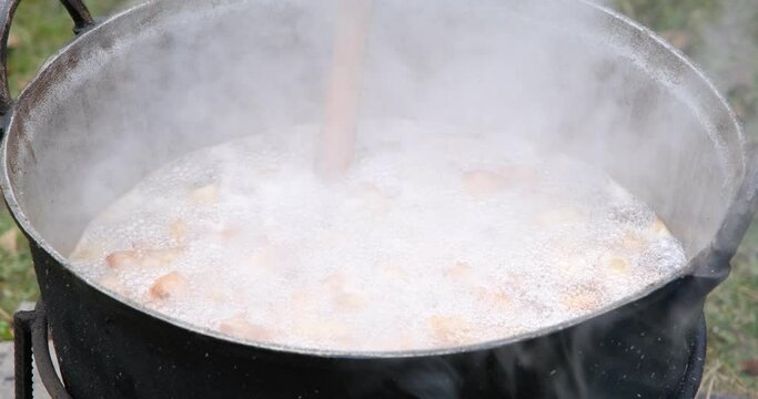 Preparation of delicious unhealthy fried pork greaves in a cauldron on the open fire. Delicious fried pork greaves in the pan traditional Romanian Christmas dish. Crispy deep fried