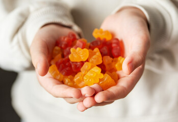 A girl holds a gummy bear vitamines in her hands - obrazy, fototapety, plakaty