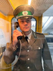 An East Berlin border guard in a telephone booth at the airport. German Democratic Republic. GDR.
