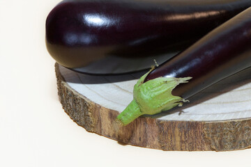 Two ripe eggplants close up on a wooden stand, on a light background